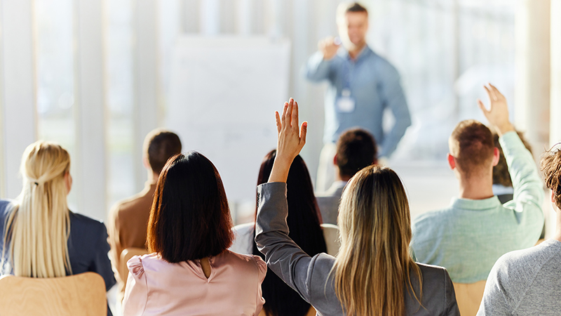 Rear view of a businesswoman raising her hand to ask a question on an education event in board room.