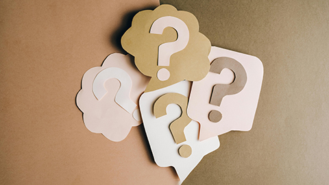Image of cut out cards with question marks against a tan background.