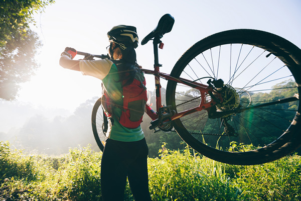A woman facing the sun on a mountain with a mountain bike over her shoulder