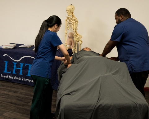 Two massage therapists tend to a client on a table.