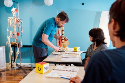 Massage therapy instructor Michael Jacobus points to the lesser trochanter on a skeleton for students to see.
