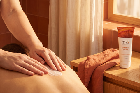 A massage therapist's hands work on a client's back, while a bottle of Myco Clinic cream rests on a stand nearby.