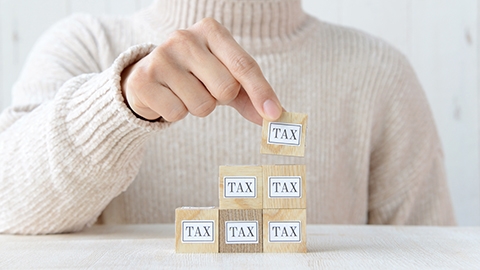 Image of a person stacking wooden blocks that say tax.