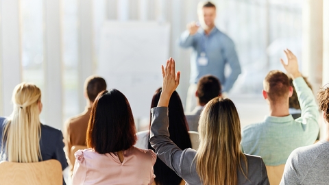 Rear view of a businesswoman raising her hand to ask a question on an education event in board room.